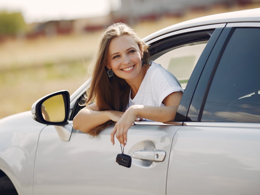 Mujer sonriendo apoyada en la ventana de su carro con las llaves en la mano